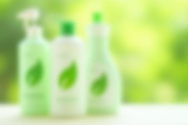 Green cleaning products on a clean surface with a leafy background, signifying eco-friendliness